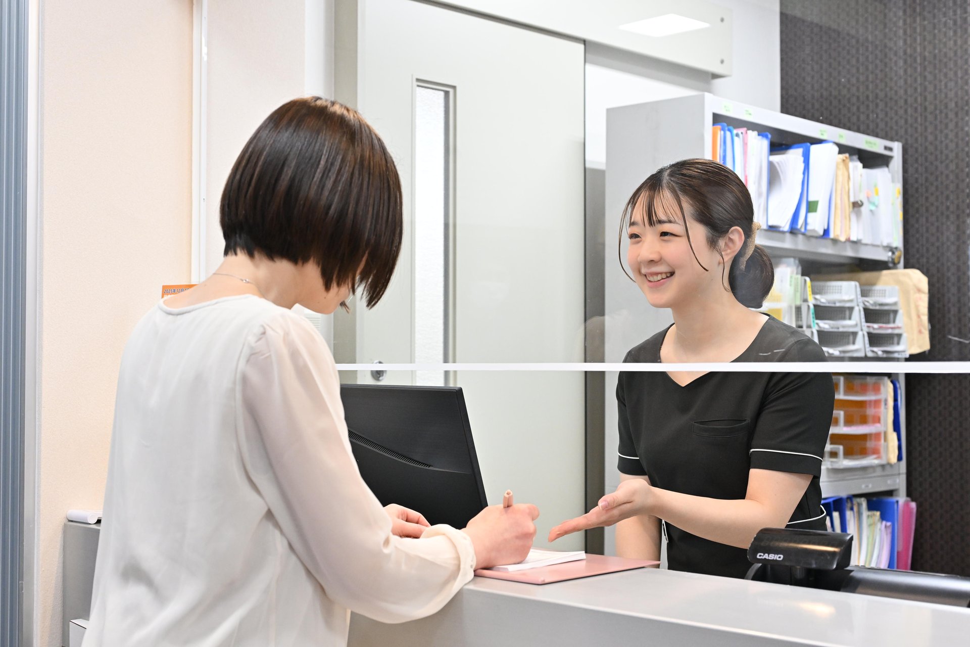 受付スタッフが患者にPC操作しながら案内する様子