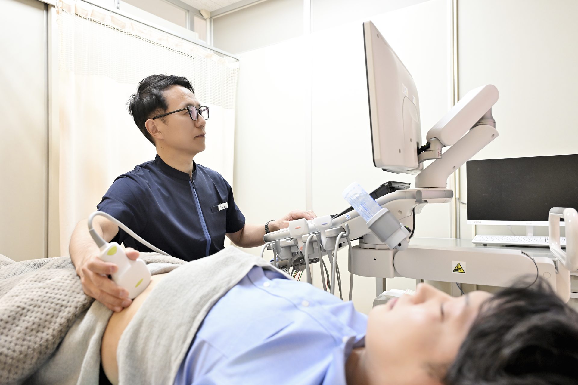 院長がエコー機器で患者の腹部を検査している様子